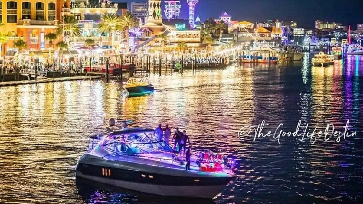 Colorful city waterfront at night with lit-up boat and buildings reflecting on water.
