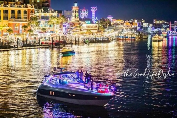 Colorful city waterfront at night with lit-up boat and buildings reflecting on water.