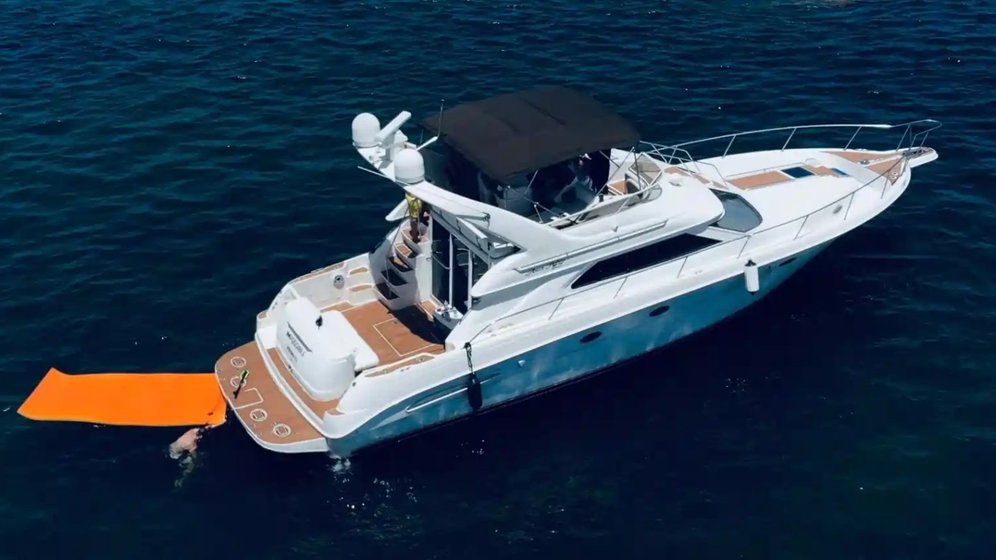 Aerial view of a yacht with an orange water mat on the ocean.