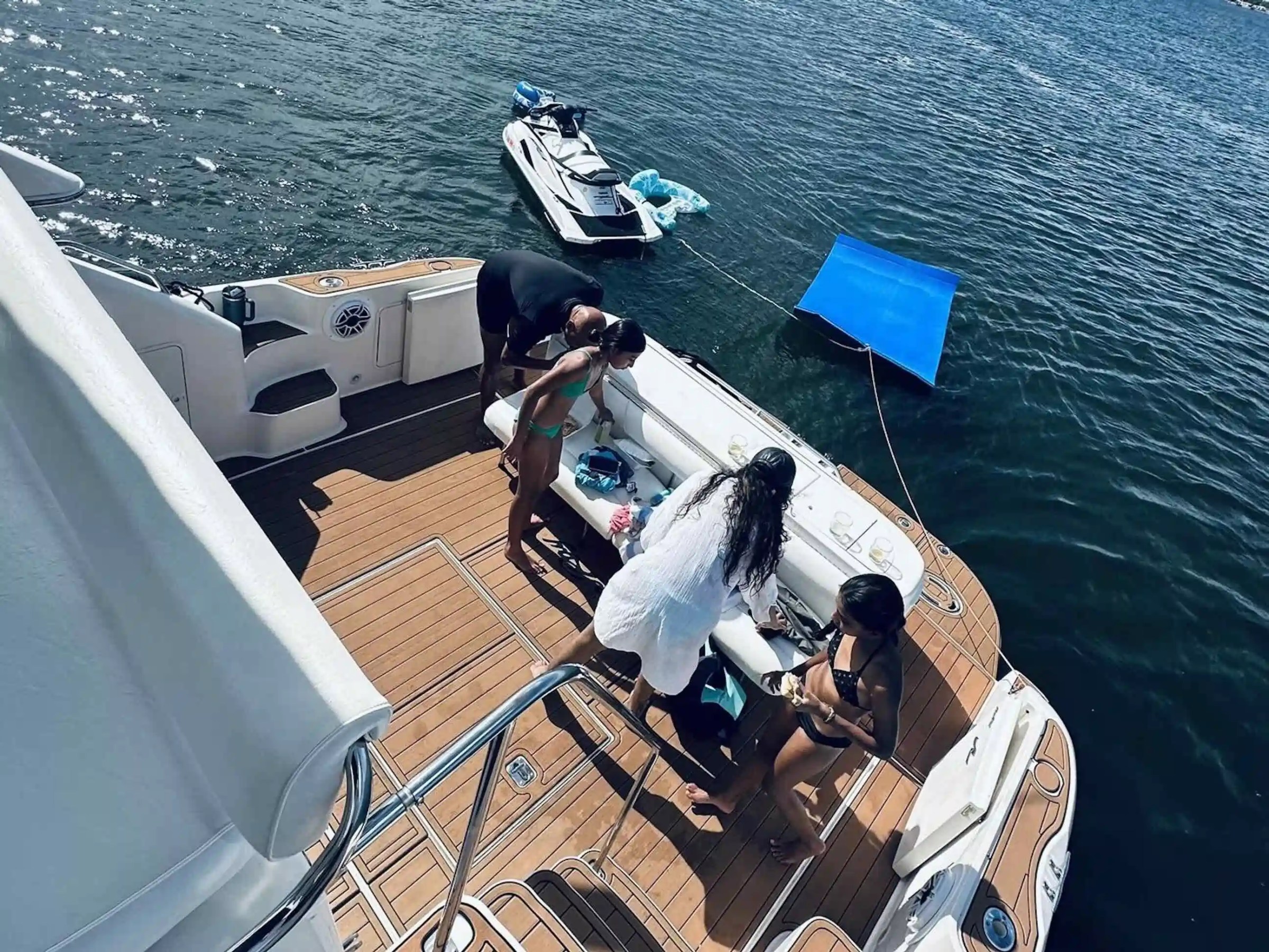 People on a boat deck with a docked jet ski, near calm water.