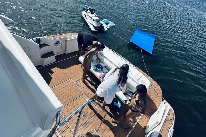 People on a boat deck with a docked jet ski, near calm water.