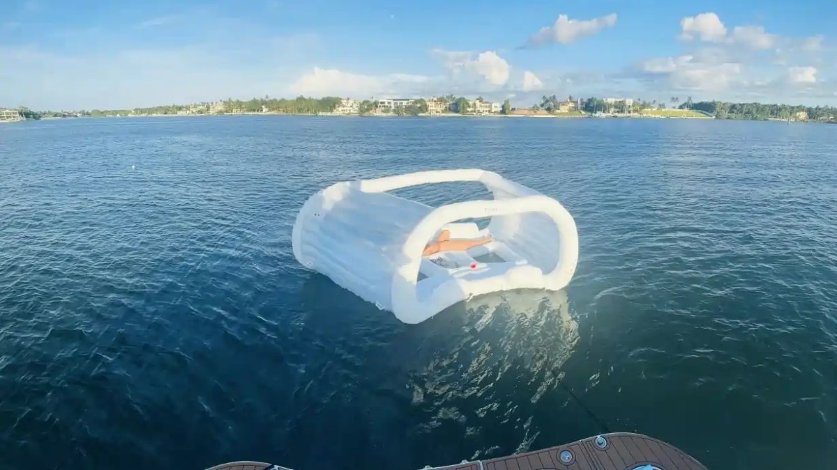 Inflatable cabana floating on blue water near a boat with distant shoreline and houses.
