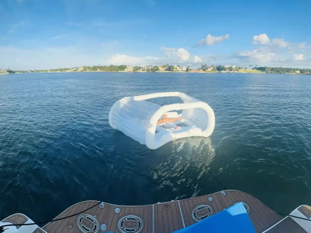 Inflatable cabana floating on blue water near a boat with distant shoreline and houses.