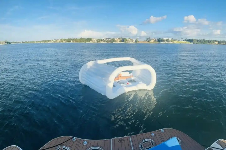 Inflatable cabana floating on blue water near a boat with distant shoreline and houses.