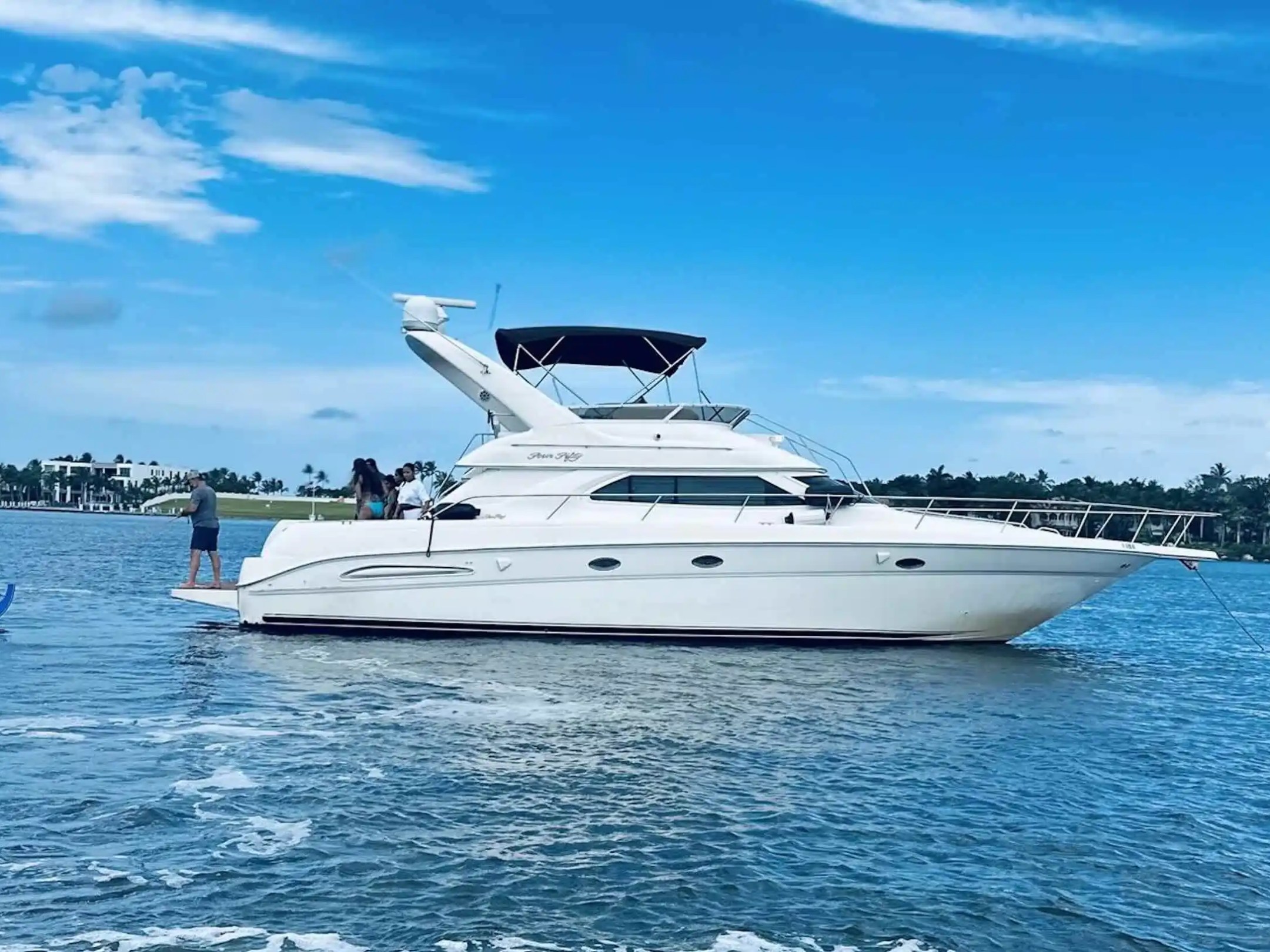 White yacht on water with people onboard against a blue sky backdrop.