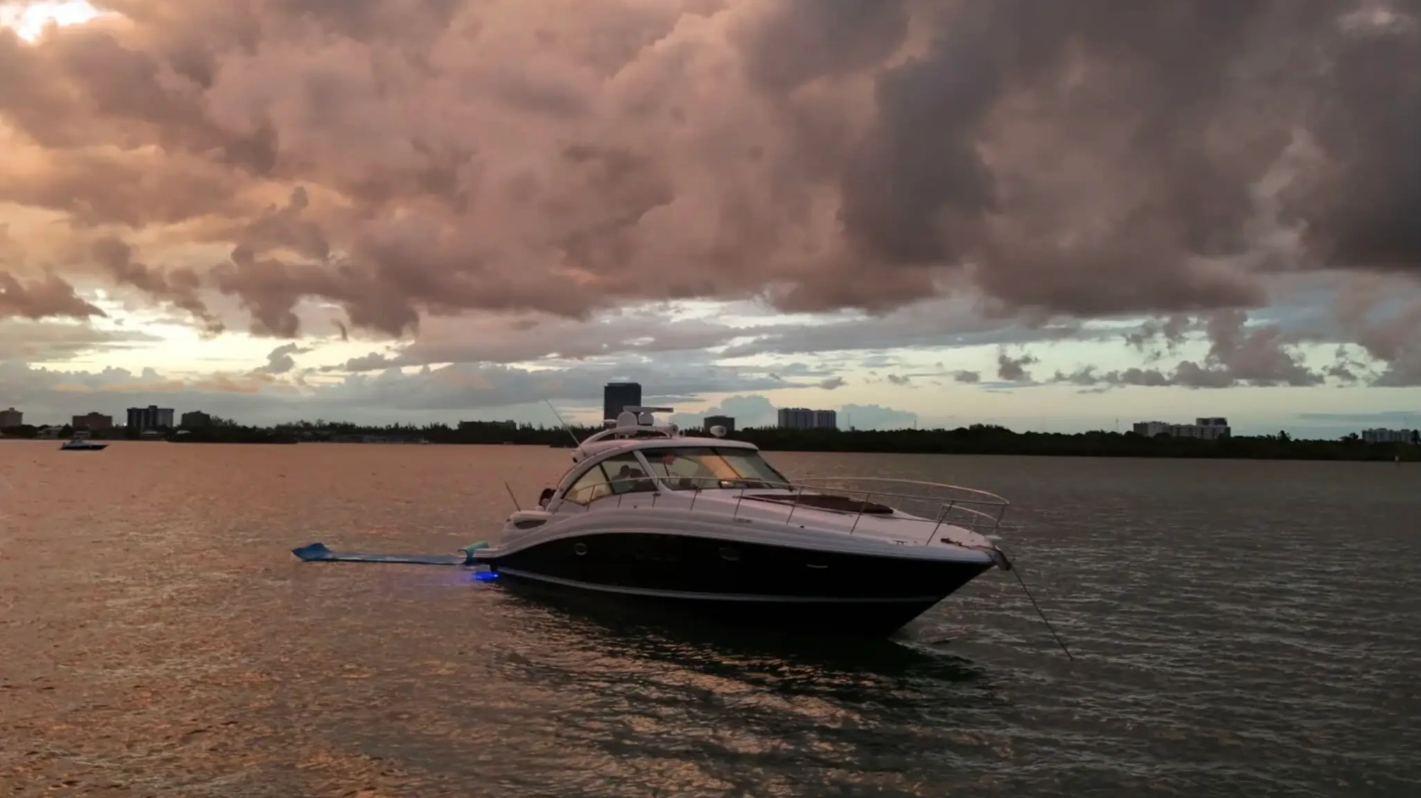 A yacht anchored on calm water under a dramatic cloudy sky during sunset.