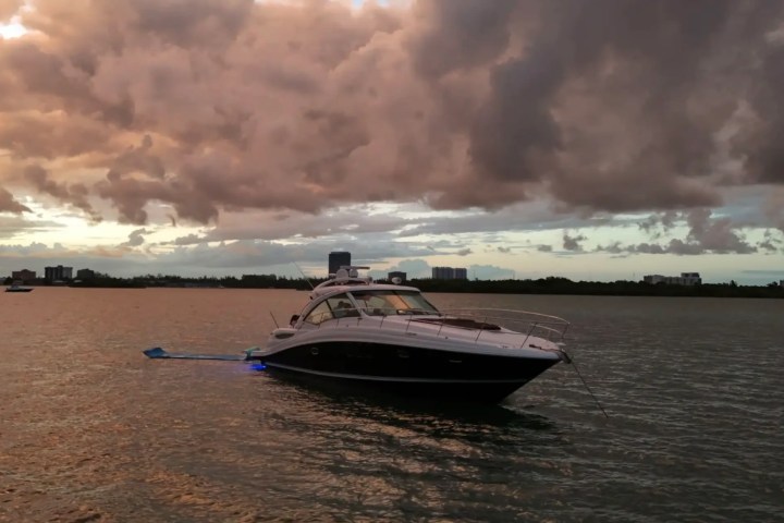 A yacht anchored on calm water under a dramatic cloudy sky during sunset.