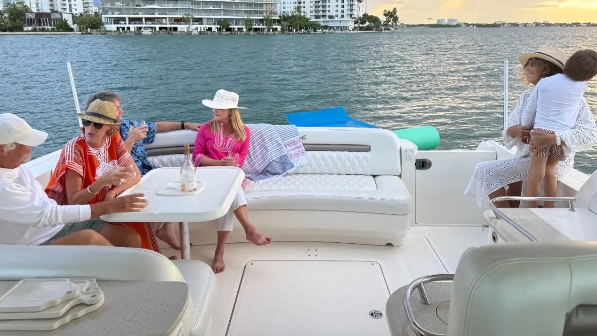 People relaxing on a boat, talking and enjoying the view of the water and distant buildings.
