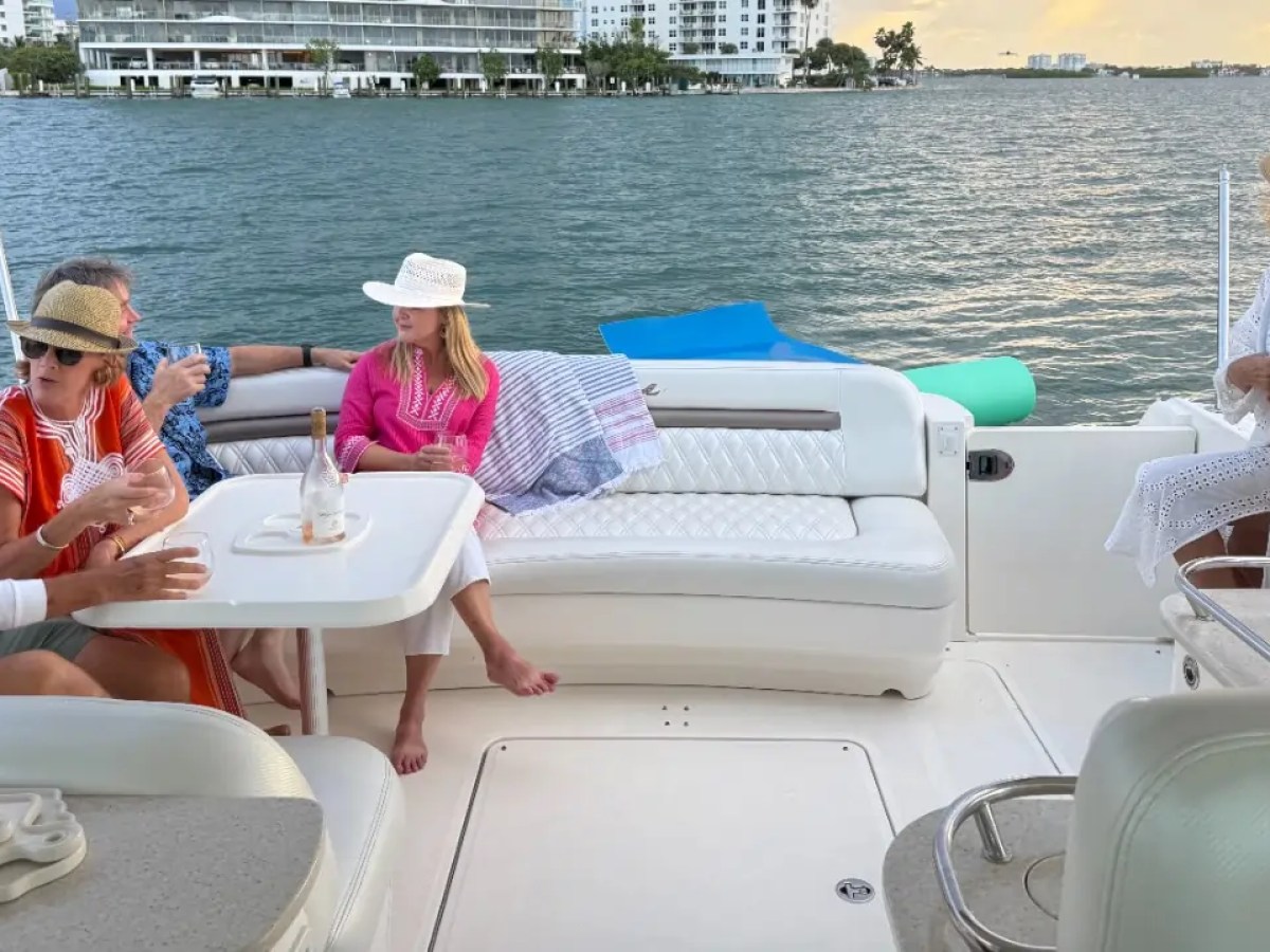 People relaxing on a boat, talking and enjoying the view of the water and distant buildings.
