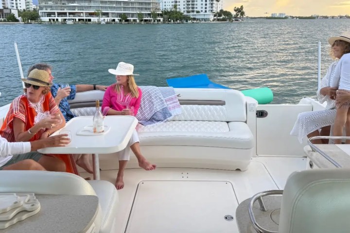 People relaxing on a boat, talking and enjoying the view of the water and distant buildings.