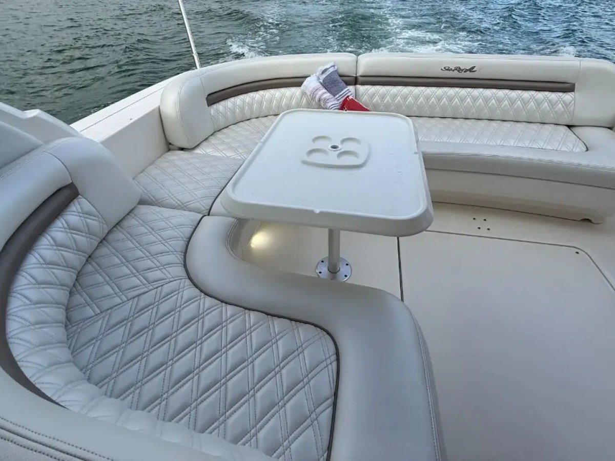 Boat interior with white cushioned seating and small table by the water.