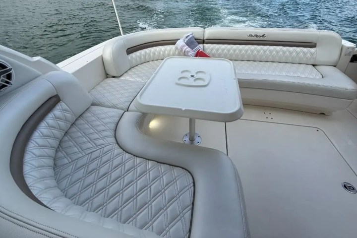 Boat interior with white cushioned seating and small table by the water.