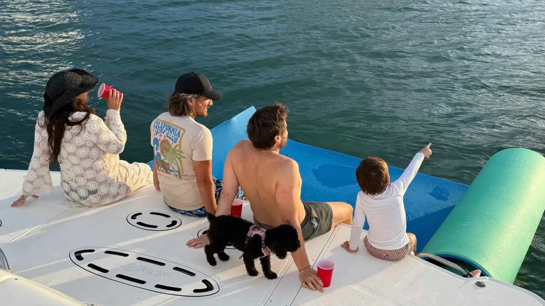 Four people and a dog relaxing on a boat, with the ocean in the background.