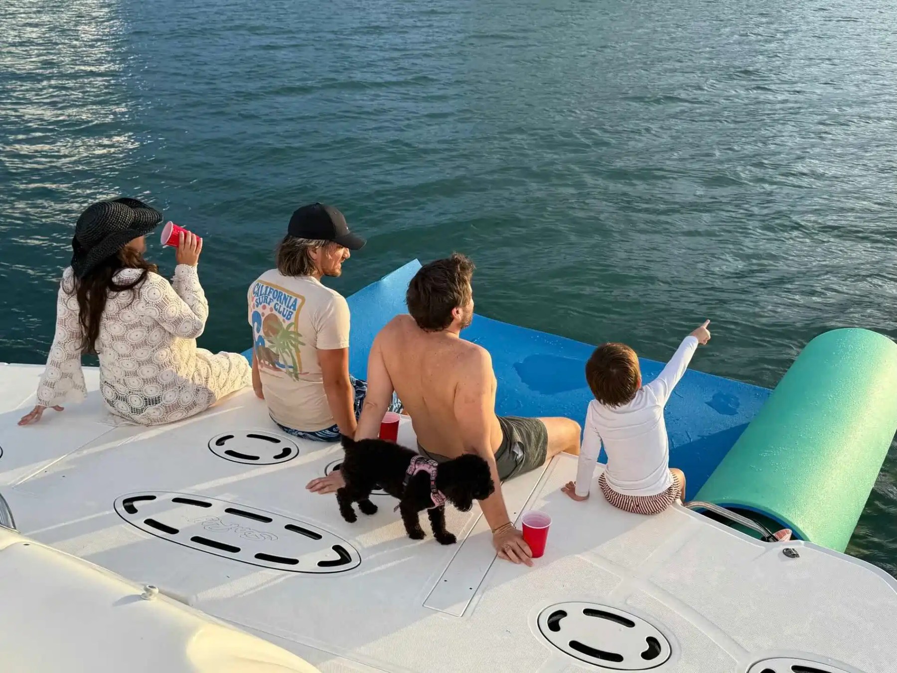 Four people and a dog relaxing on a boat, with the ocean in the background.