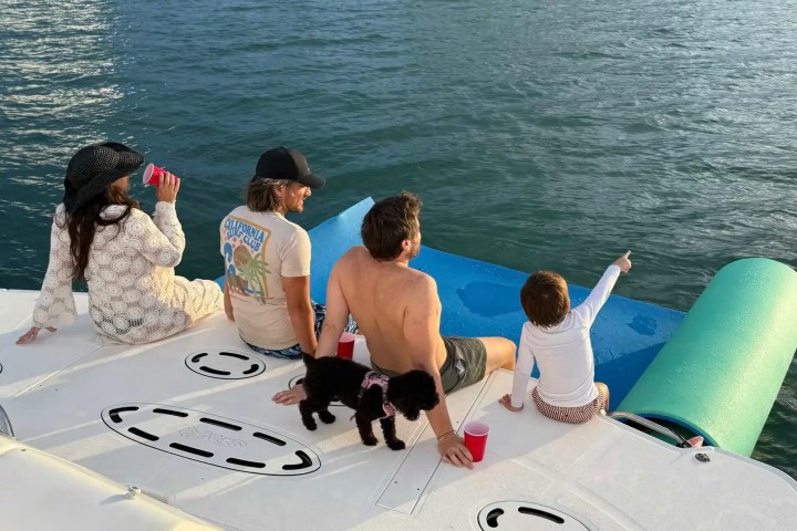 Four people and a dog relaxing on a boat, with the ocean in the background.