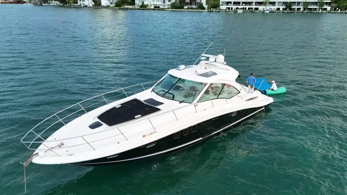 A yacht on water with two people standing on a floating platform beside it.