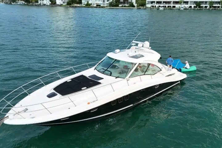 A yacht on water with two people standing on a floating platform beside it.