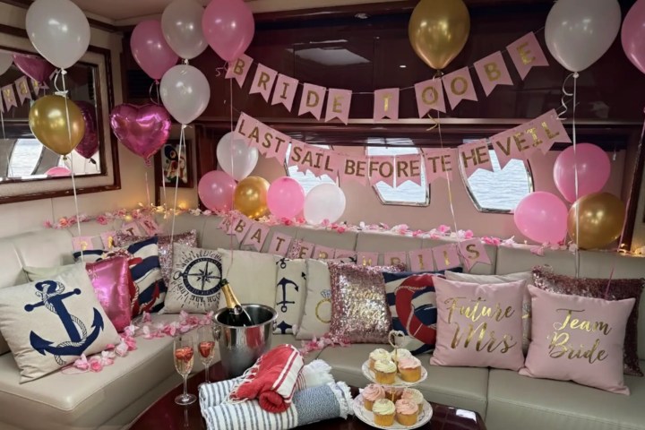 Nautical-themed bridal shower with balloons, pillows, cupcakes, and champagne on a boat.