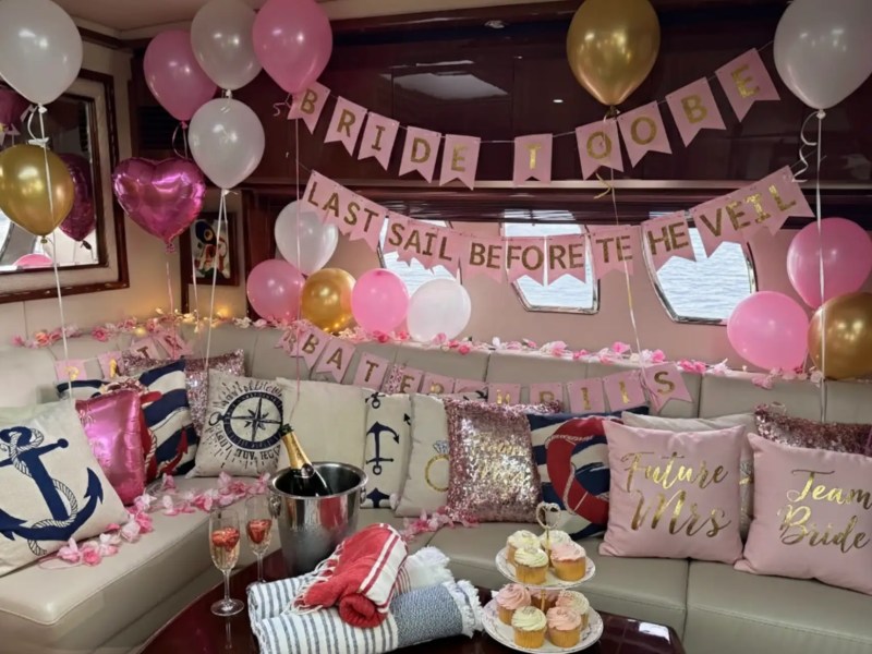 Nautical-themed bridal shower with balloons, pillows, cupcakes, and champagne on a boat.