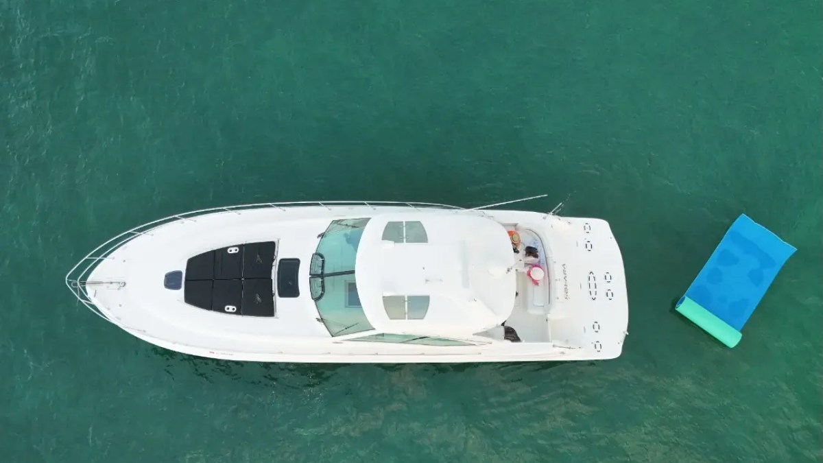 Top view of a white yacht on clear water with a blue raft nearby.