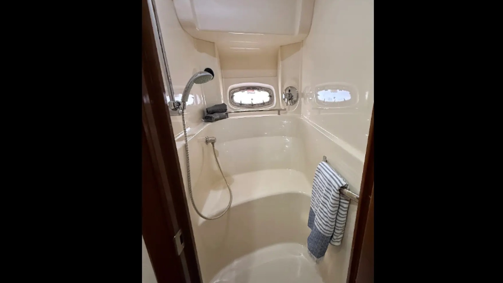 Narrow boat bathroom with shower, porthole window, towel rack, and striped towel.