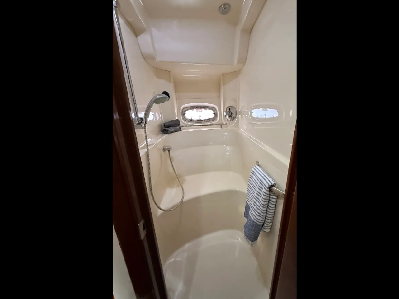 Narrow boat bathroom with shower, porthole window, towel rack, and striped towel.