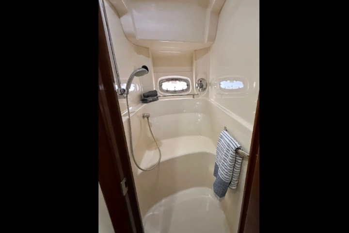 Narrow boat bathroom with shower, porthole window, towel rack, and striped towel.