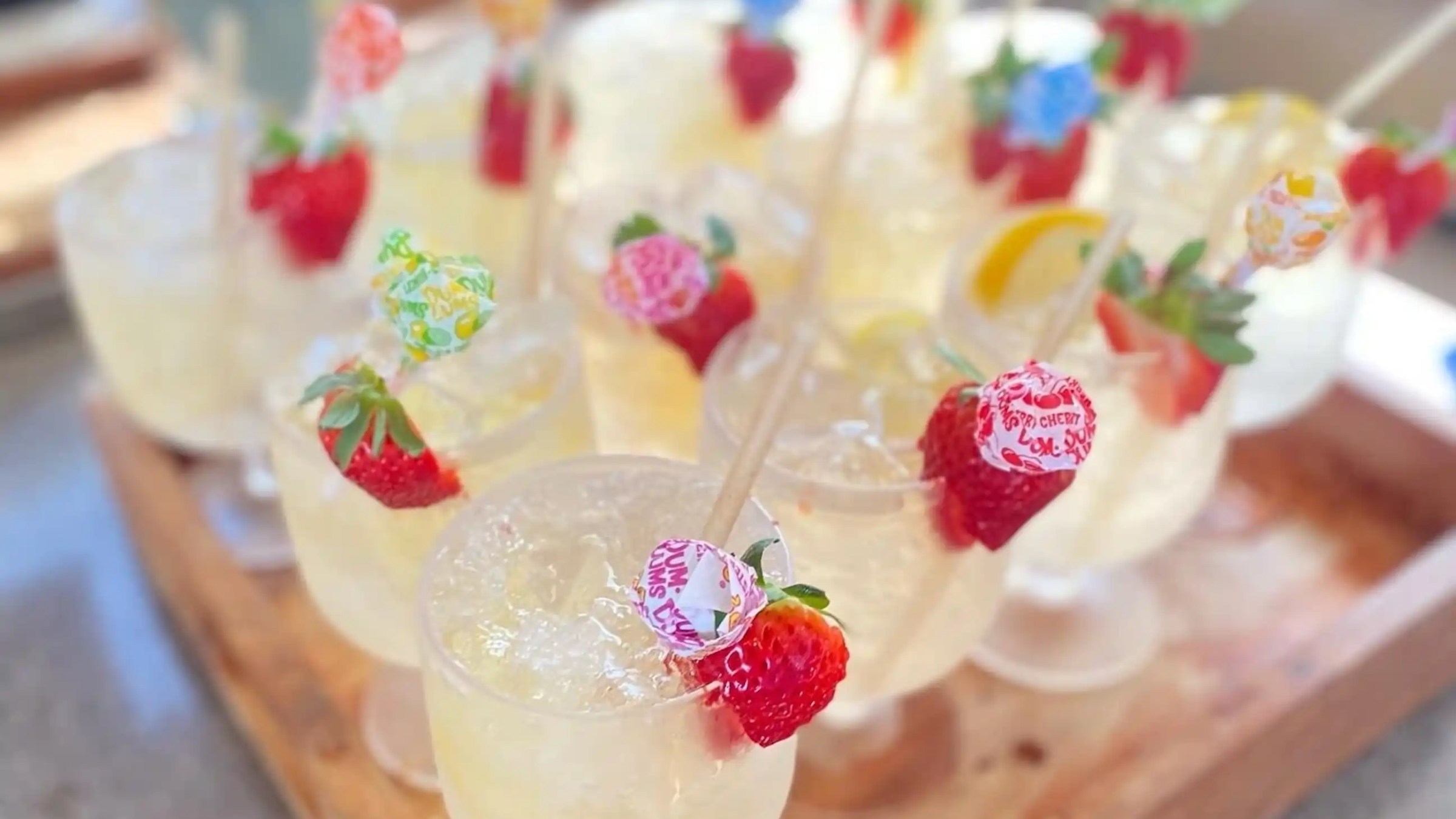 Glasses of lemonade with strawberries and lollipops on sticks as garnish.