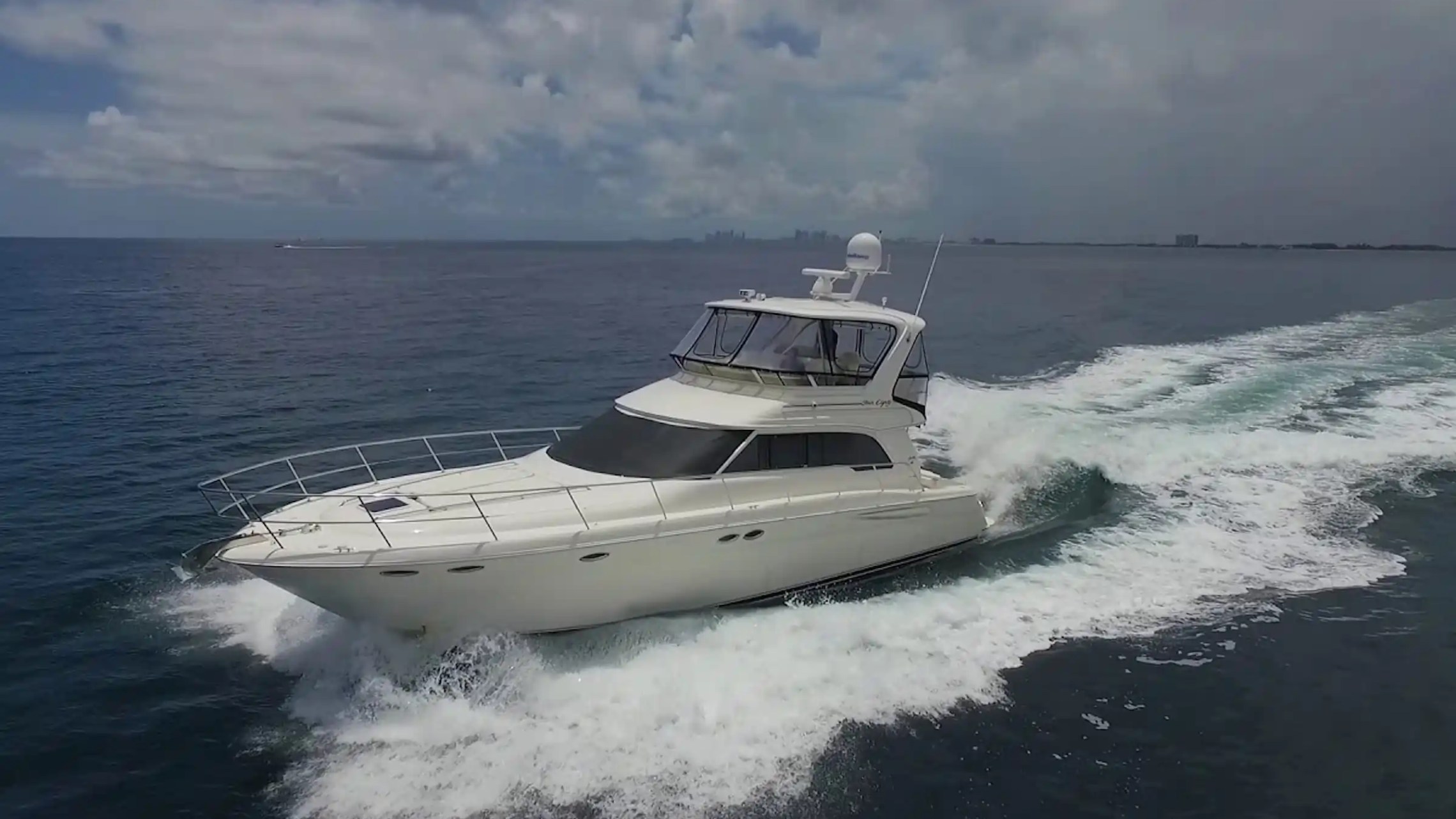 Large white yacht cruising on open water under a cloudy sky.