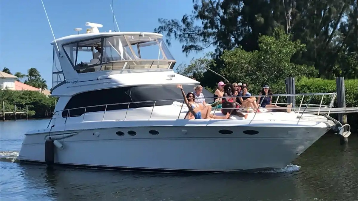 Group of people relaxing on a yacht cruising near green trees and houses.