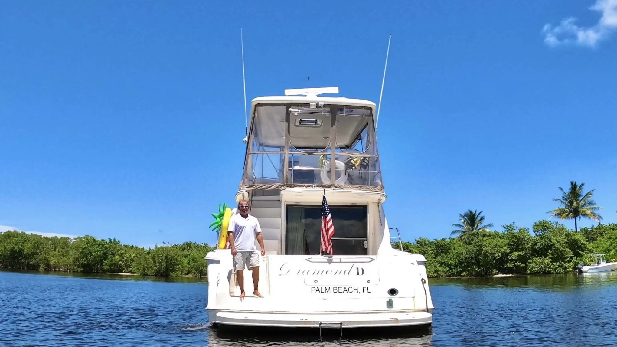 Man standing on the back of a boat with an American flag, on a sunny day.