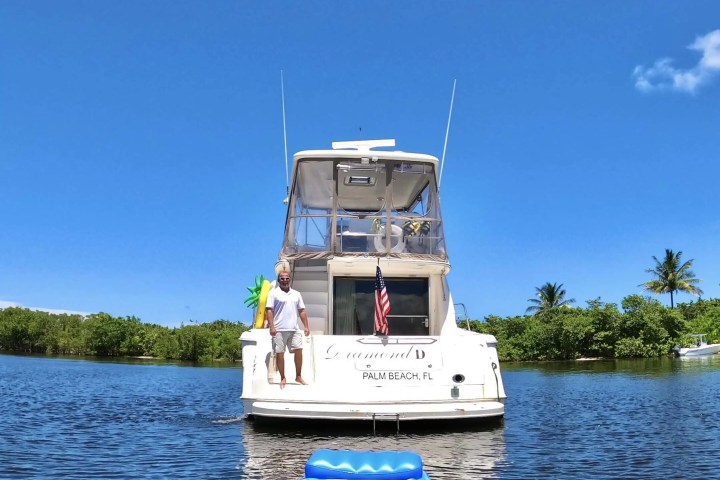 Man standing on the back of a boat with an American flag, on a sunny day.