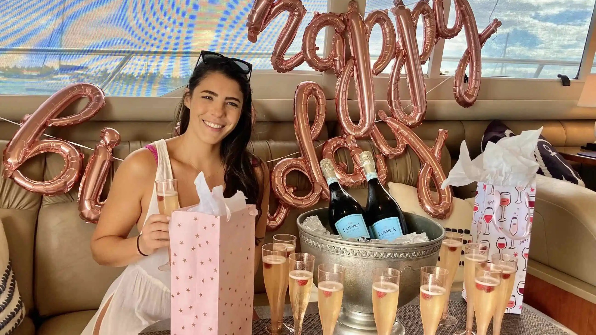 Woman celebrates birthday on yacht with balloons, champagne, and gifts.
