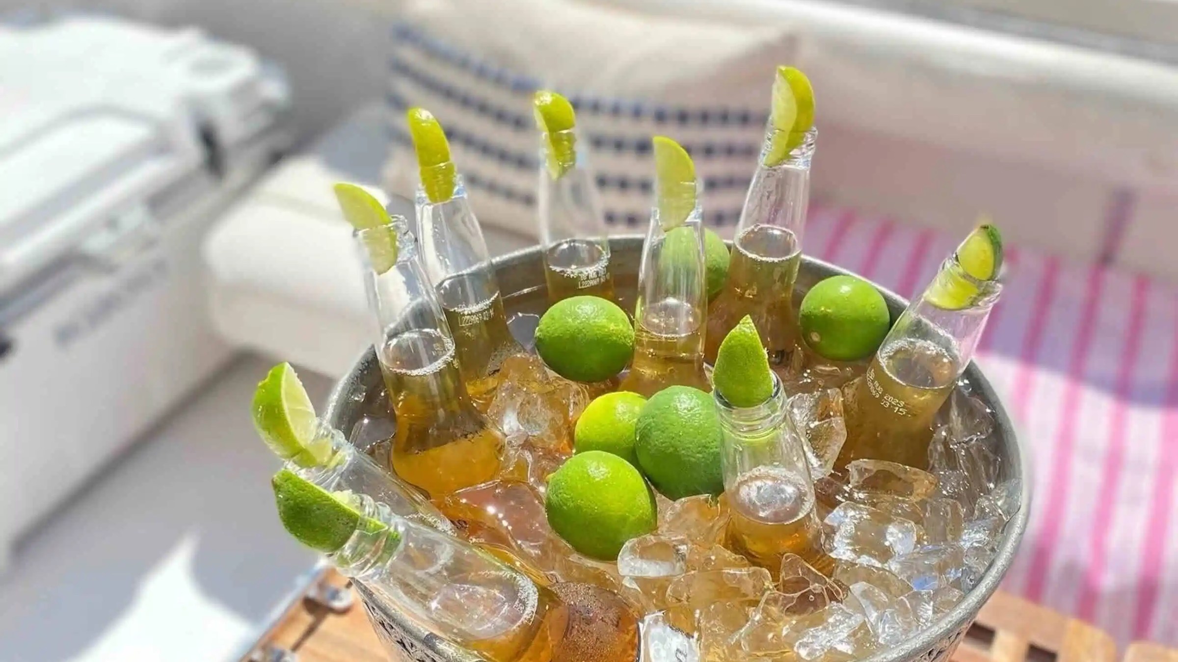 Ice bucket with beer bottles and lime wedges on a wooden table.