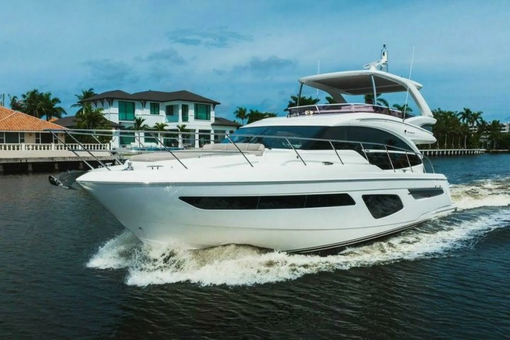 White yacht cruising on a canal with houses and palm trees in the background.