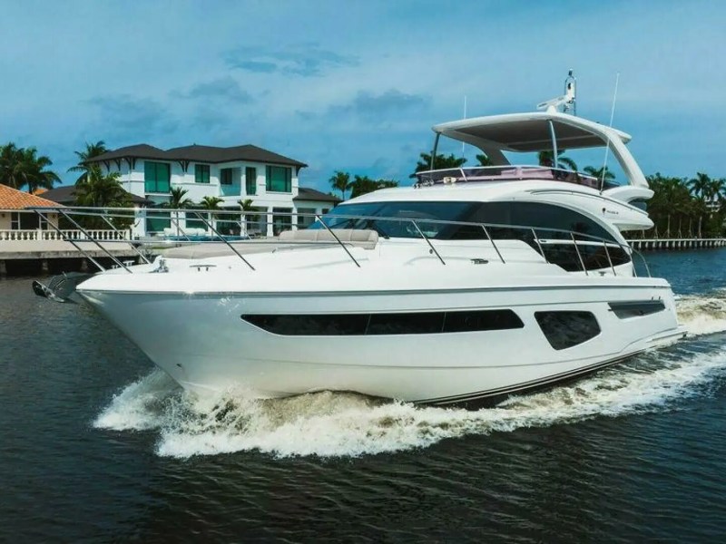 White yacht cruising on a canal with houses and palm trees in the background.