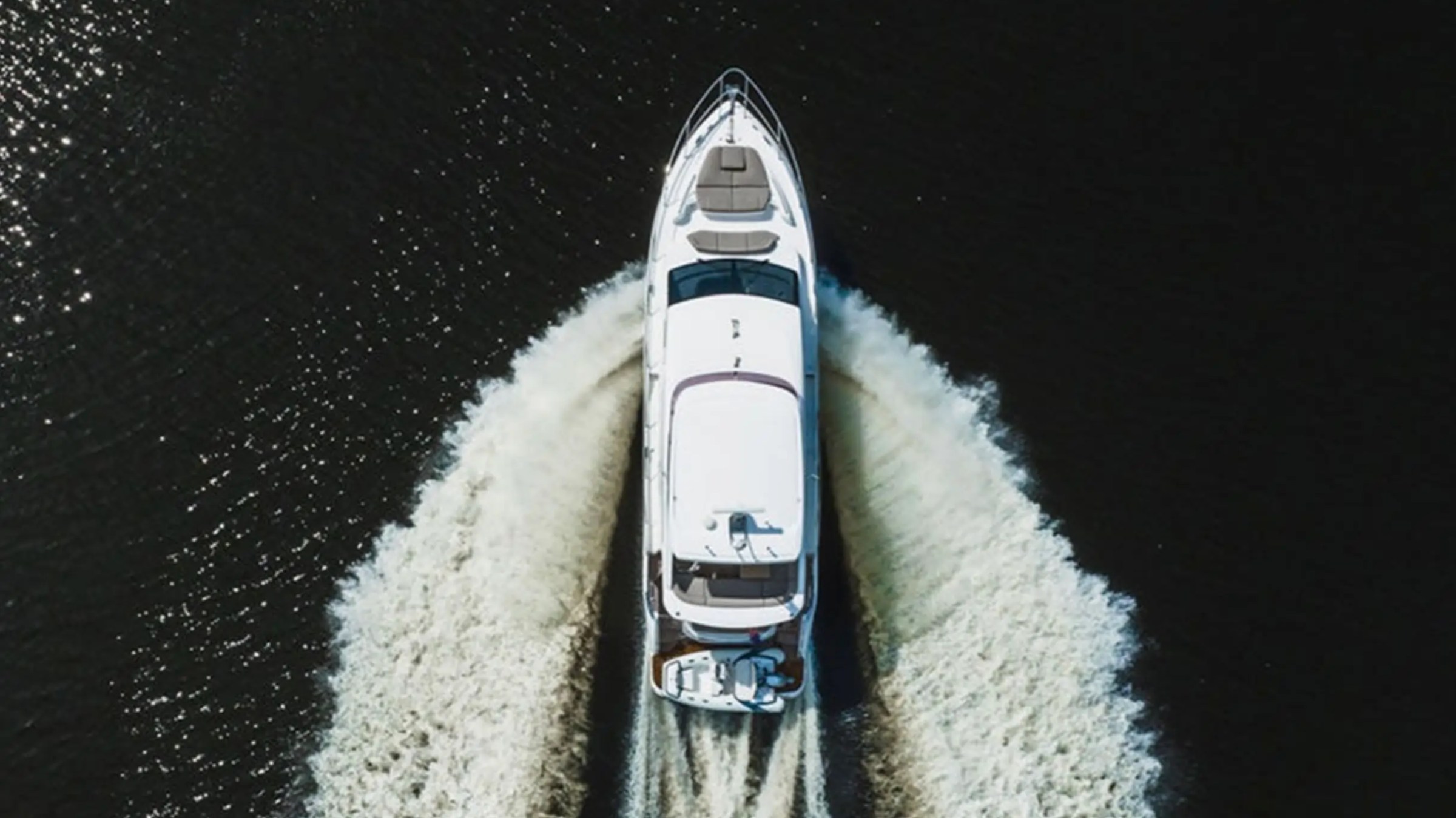 Overhead view of a white yacht making a V-shaped wake on dark water.