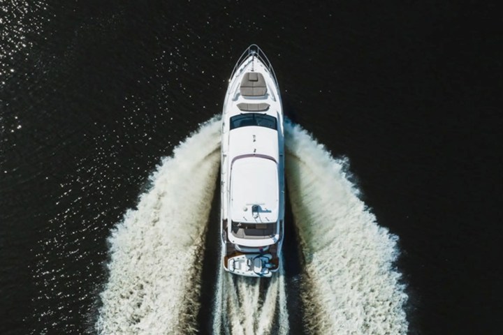 Overhead view of a white yacht making a V-shaped wake on dark water.