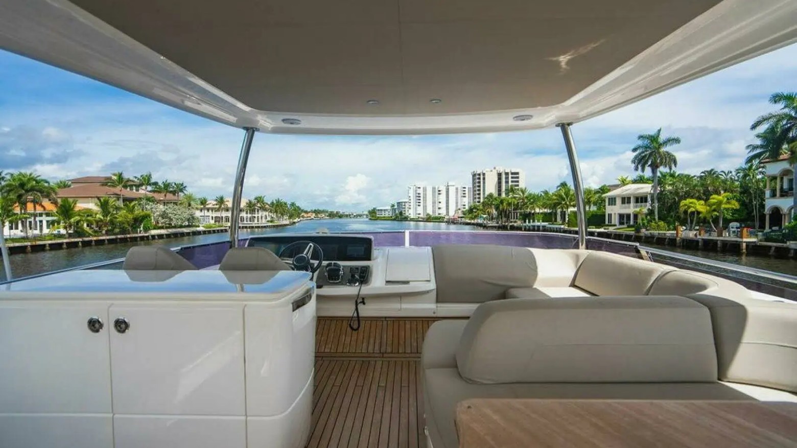 Luxury yacht deck with modern seating, overlooking a waterfront cityscape with palm trees and buildings.