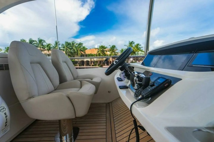 Luxury yacht interior with two beige seats and boat controls under a sunny sky with palm trees.