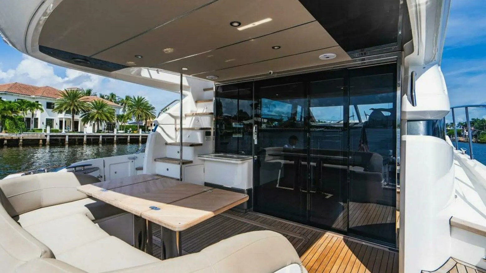 Outdoor deck of luxury yacht with seating and table, against a waterfront background.