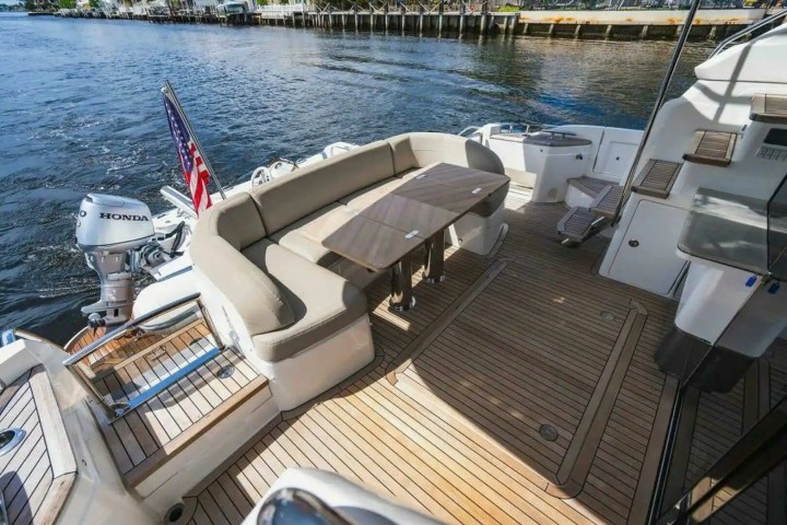 Boat deck with wooden flooring, curved seating, table, and an American flag near the water.
