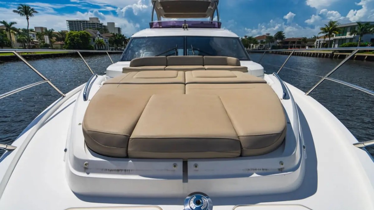 Luxury yacht deck with beige cushioned sunbed on a sunny day, cityscape in background.