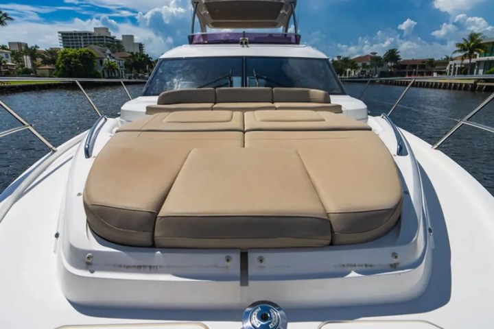 Luxury yacht deck with beige cushioned sunbed on a sunny day, cityscape in background.