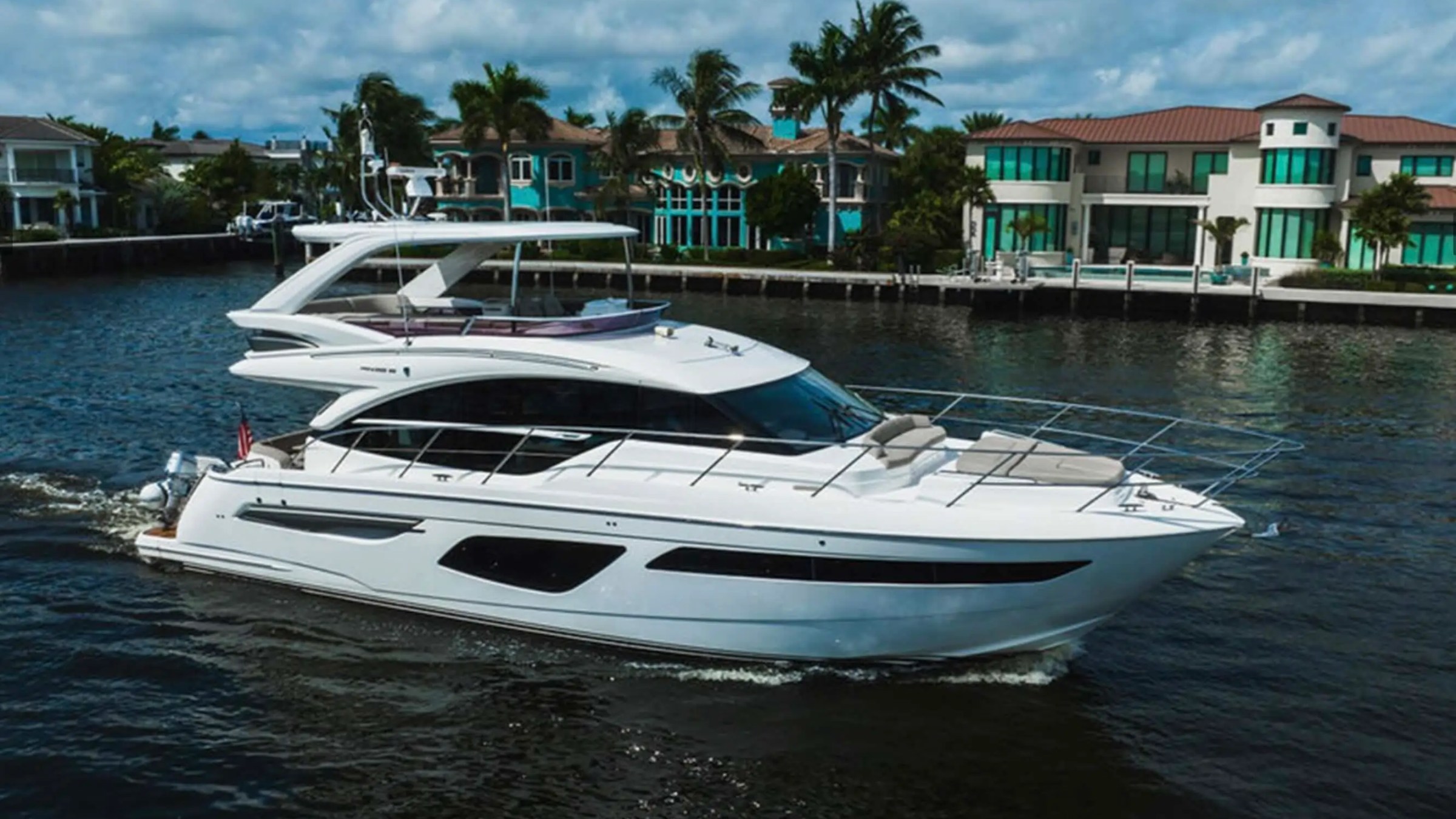 Luxury yacht sailing near waterfront homes with palm trees.