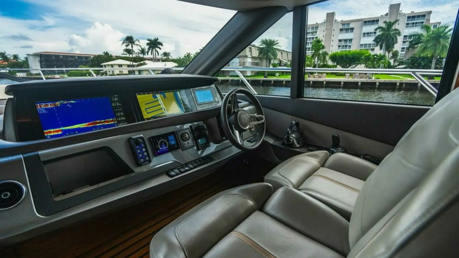 Boat cockpit with modern controls and large windows showing a canal and palm trees.