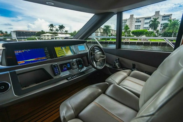 Boat cockpit with modern controls and large windows showing a canal and palm trees.