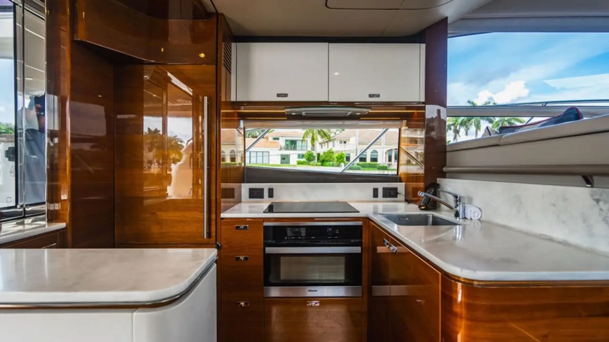 Luxury boat kitchen with glossy wood cabinets, white countertops, and view of water through large windows.