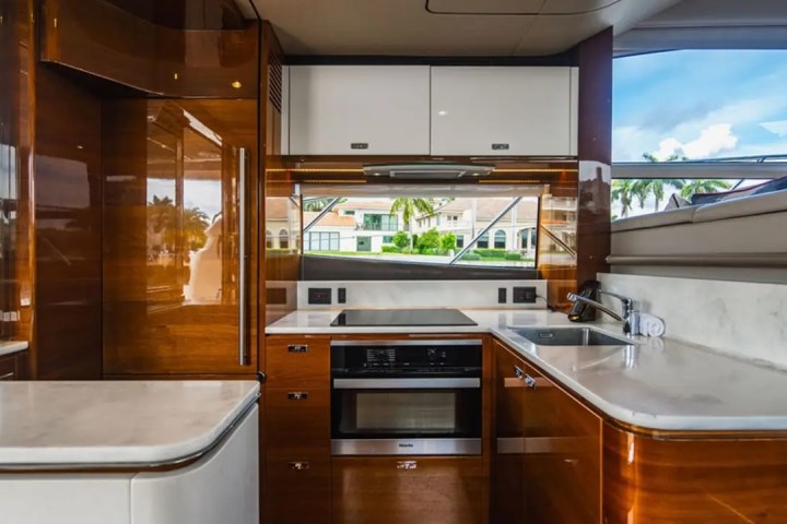 Luxury boat kitchen with glossy wood cabinets, white countertops, and view of water through large windows.