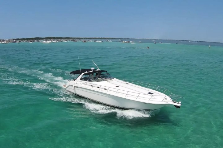 White yacht cruising on turquoise water near a crowded beach.